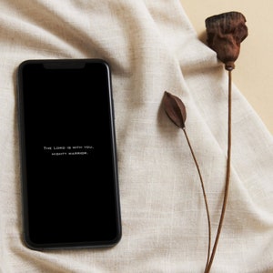 Könnte beinhalten: Ein schwarzes Smartphone mit weißem Hintergrund, auf dem der Text "The Lord is with you, Mighty Warrior." angezeigt wird.