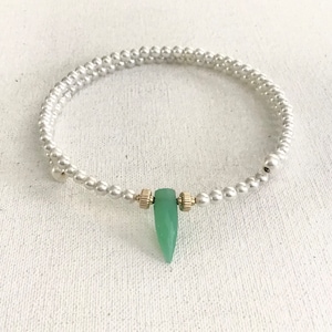 May include: A delicate white pearl bracelet with a single green gemstone pendant. The bracelet is made of small, round pearls and has a simple, elegant design.