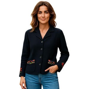 May include: A black blazer with a notched collar and three buttons. The blazer has two front pockets and floral embroidery on the pockets and left sleeve. The person is wearing blue jeans.