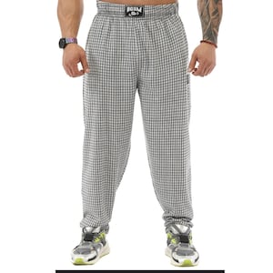 Puede incluir: Pantalones a cuadros grises y blancos con una cinturilla negra con el texto "BGSM". Los pantalones tienen un corte holgado y se combinan con zapatillas deportivas grises y verde neón. El estilo general es casual y deportivo.