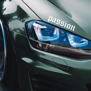 Könnte beinhalten: Ein grünes Auto mit einem weißen Aufkleber, auf dem "passion" auf dem vorderen Kotflügel steht. Das Auto hat eine schwarze Frontstoßstange und einen schwarzen Kühlergrill.