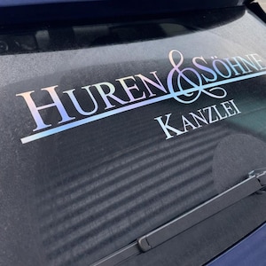 Könnte beinhalten: Ein Autoaufkleber mit dem Text "Huren & Söhne Kanzlei" in einer stilisierten Schriftart. Der Text hat einen Farbverlauf, und der Aufkleber ist auf der Heckscheibe eines blauen Autos angebracht.