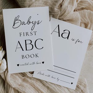 Puede incluir: Dos tarjetas rectangulares blancas con texto en negro. La primera tarjeta dice Baby's FIRST ABC BOOK created with love. La segunda muestra Aa is for con una línea en blanco y el texto Made with love by seguido de una línea y un corazón.