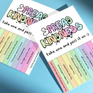 May include: Two white cards with the words "SPREAD KINDNESS" in colorful bubble letters. Each card has a list of positive affirmations in pastel colors. The text "take one and pass it on :)" is also visible.