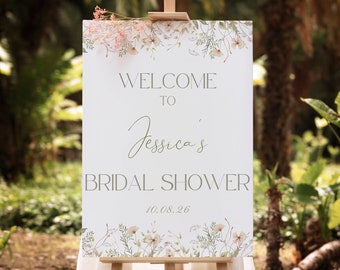 May include: A white welcome sign with green floral accents and the text "Welcome to Jessica's Bridal Shower 10.08.26". The sign is on an easel in a garden setting.