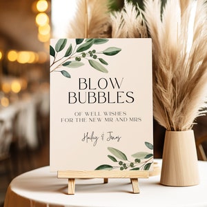 May include: A sign with a light brown background and green foliage with berries. The sign reads "Blow Bubbles of well wishes for the new Mr. and Mrs. Hailey & Jonas".