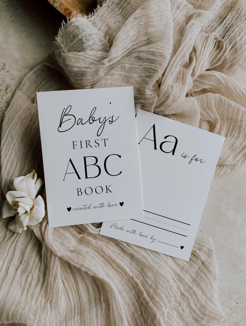 May include: Two white rectangular cards with black text. The first card reads Baby's FIRST ABC BOOK created with love. The second card shows Aa is for with a blank line and the text Made with love by followed by a blank line and a small heart icon.