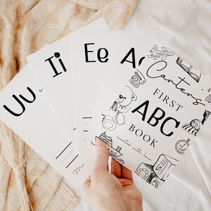 May include: A set of black and white flashcards with letters of the alphabet. The cards feature illustrations of various objects, including a teddy bear, a plane, a phone, and a rain cloud. The text on the cards reads "Carter's First ABC Book, created with love."
