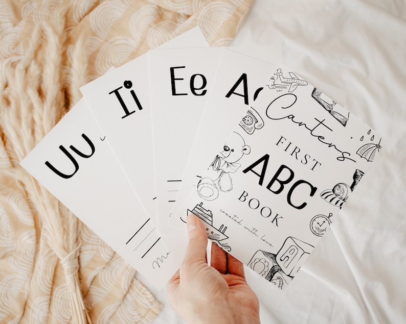 May include: A set of black and white flashcards with letters of the alphabet. The cards feature illustrations of various objects, including a teddy bear, a plane, a phone, and a rain cloud. The text on the cards reads "Carter's First ABC Book, created with love."
