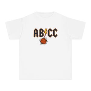 May include: A white short-sleeve t-shirt featuring a graphic print on the chest. The design displays the text AB/CC in dark blue with orange outlines, separated by a yellow lightning bolt. Below, an orange basketball appears to crack the surface.