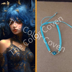 May include: A light blue adjustable bracelet with a gold evil eye charm. The bracelet is made with a knotted cord and has gold beads on either side of the charm.