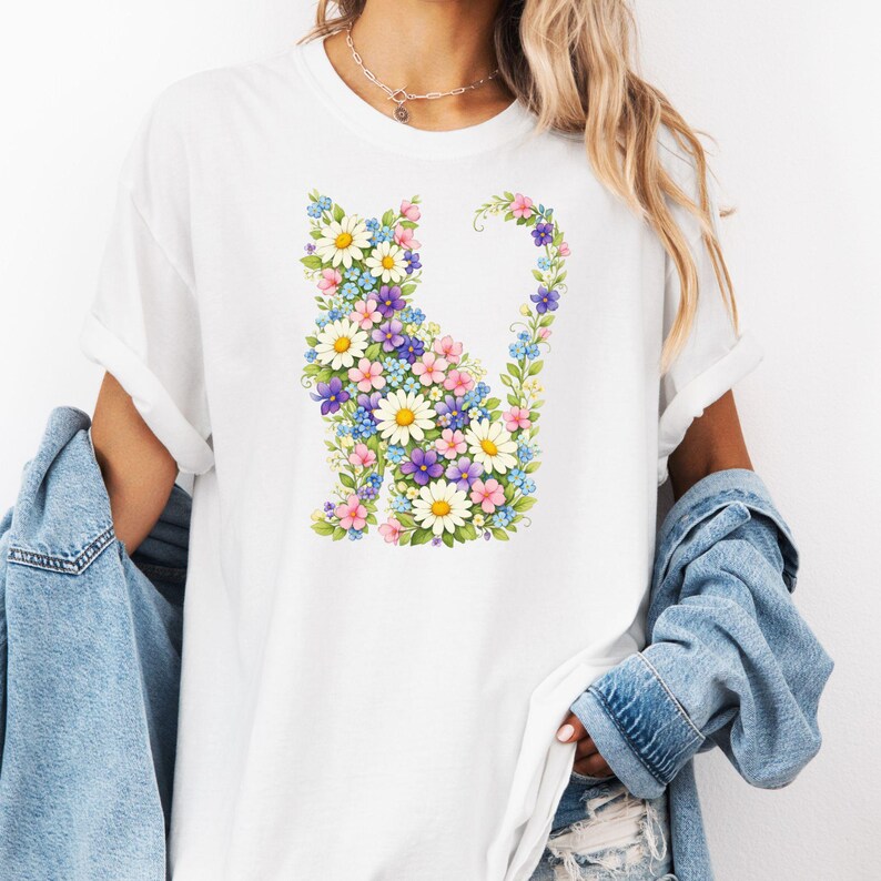 May include: White t-shirt featuring a floral cat design. The cat silhouette is composed of colorful flowers, including daisies, purple, pink, and blue blooms. The shirt has short sleeves and a relaxed fit.