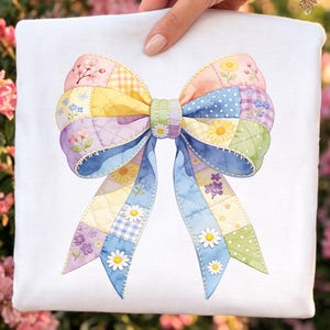 May include: A colorful, patchwork bow design with floral accents. The bow features a variety of pastel colors, including pink, yellow, blue, and green, with a quilted texture. Daisies and other flowers are scattered across the bow's surface.