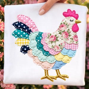 May include: A white square fabric with a colorful appliqued rooster design. The rooster features a pink comb and wattle, a floral patterned body, and a tail with polka dots and gingham. The rooster's legs are gold, and the design is stitched.