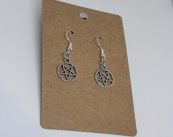 May include: A pair of silver-toned dangle earrings featuring a circular pentagram charm. Each earring is attached to a silver-colored hook wire and is displayed on a rectangular brown cardboard backing card with a hole at the top for hanging.