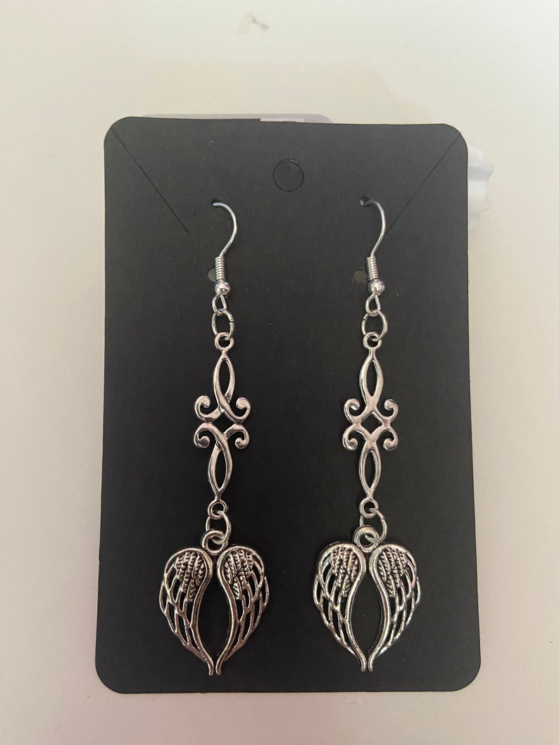 May include: A pair of silver dangle earrings with a delicate filigree design and angel wing charms.