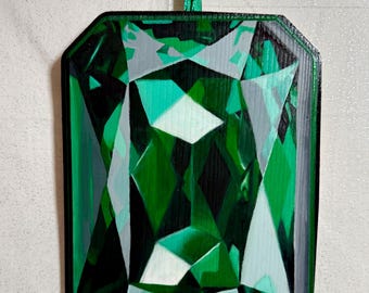 Può includere: Dipinto di una gemma rettangolare taglio smeraldo con bordo verde scuro. L'opera presenta sfumature di verde, bianco e grigio, creando un aspetto sfaccettato simile a una gemma. Un nastro verde è attaccato per appenderlo.