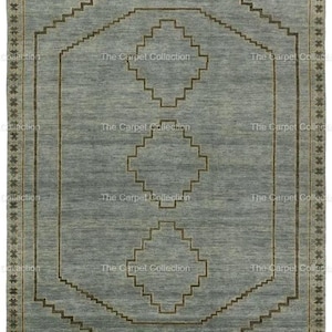 May include: A rectangular, light blue rug with a geometric design. The rug features a central pattern of diamonds and stepped lines in a darker brown color. The border is a repeating star pattern. The text "The Carpet Collection" is repeated around the edges.