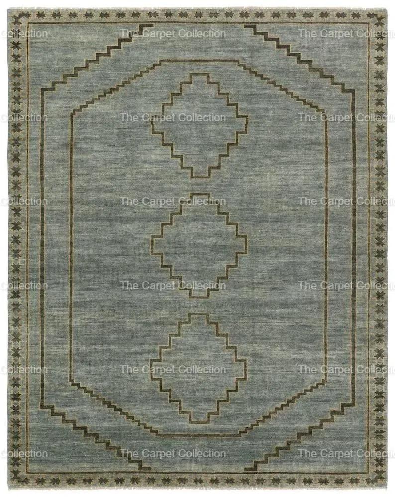 May include: A rectangular, light blue rug with a geometric design. The rug features a central pattern of diamonds and stepped lines in a darker brown color. The border is a repeating star pattern. The text "The Carpet Collection" is repeated around the edges.