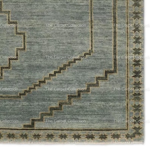 May include: Close-up of a rectangular rug with a geometric design. The rug features a light blue background with dark brown stepped patterns and a border with star-like motifs. The text "The Carpet Collection" is visible.