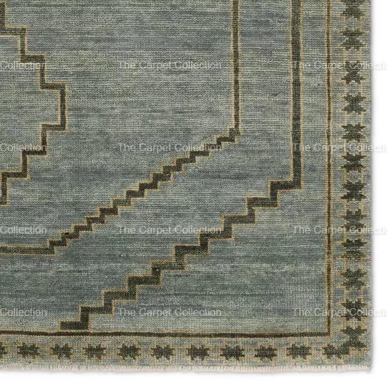 May include: A close-up of a blue and brown area rug with a geometric pattern. The rug features a stepped design in dark brown and a border with star-like shapes. The text "The Carpet Collection" is visible.