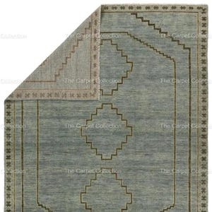 May include: A rectangular, light blue rug with a geometric pattern. The rug features a central diamond design and a border with star-like shapes. The edges are trimmed with a darker brown color, and the rug is partially folded.