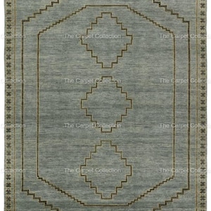 May include: A rectangular, light blue rug with a geometric design. The rug features a central pattern of diamonds and stepped lines in a darker brown color. The border has a repeating star pattern. The text "The Carpet Collection" is visible.