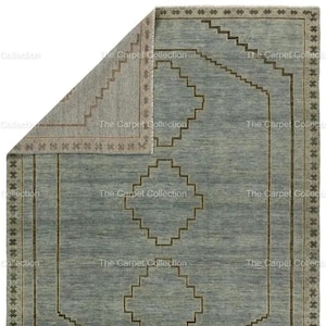 May include: A rectangular, light blue rug with a geometric pattern. The rug features a central diamond design and a border with star-like shapes. The edges are trimmed with a darker brown color, and the rug is partially folded.