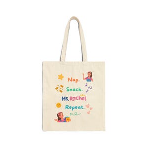 May include: Cream-colored tote bag with a design featuring the words "Nap. Snack. Ms. Rachel Repeat." along with illustrations of a star, snacks, musical notes, a sun, and hearts. The bag has two handles.
