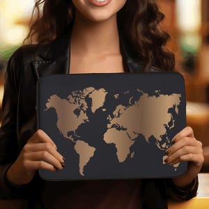 May include: A black laptop sleeve featuring a gold-colored world map design. The sleeve is rectangular and appears to be made of a durable material. The world map design is a prominent feature, with continents and countries outlined in gold.