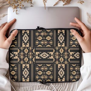 May include: A black laptop sleeve with a geometric pattern in beige, brown, and blue. The design features repeating shapes and patterns, creating a Southwestern or tribal aesthetic. The sleeve has a black zipper closure.