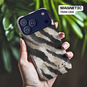 May include: A phone case with a zebra stripe pattern in shades of black, gray, and beige. The case has a dark blue camera housing and the text "MAGNETIC TOUGH CASE" in white. The initials "LS" are visible on the lower right corner.