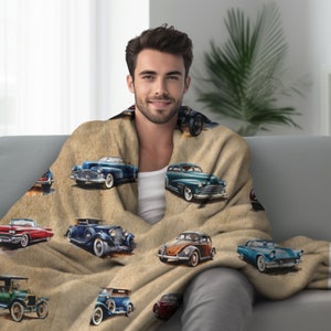 May include: A beige throw blanket with a vintage car pattern. The blanket features a variety of classic cars in different colors, including blue, red, and green. The blanket is soft and cozy, perfect for snuggling up on the couch.
