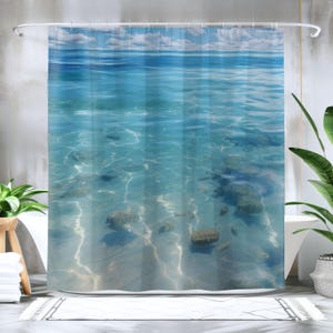 May include: A shower curtain with a blue and white ocean scene. The curtain features a view of the ocean floor with rocks and coral.