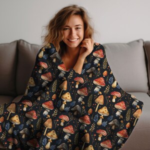 May include: A black throw blanket with a watercolor pattern of mushrooms and leaves. The blanket is soft and cozy, perfect for snuggling up on the couch.