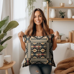 May include: A woman holds a decorative throw pillow with a geometric pattern in shades of black, gray, beige, red, blue, and yellow. The pillow has a southwestern or tribal design.
