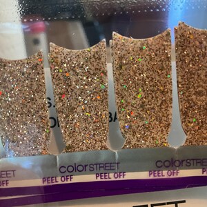 May include: Close-up of several nail polish strips with a glittery, gold finish. The strips are labeled "Color Street" and "Peel Off". The glitter has iridescent flecks.