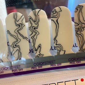 May include: A set of Color Street nail polish strips. Each strip is white with a black, abstract, wavy design. The packaging reads "colorSTREET" and "PEEL OFF".