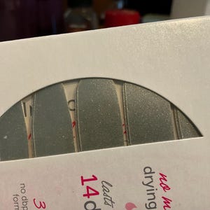 May include: A package with a semi-circular window revealing several silver nail polish strips. The package has text that reads "14 days" and "no dbp". The strips are a metallic silver color.