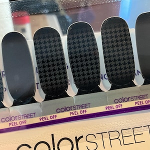 May include: Color Street nail strips in a package. The strips feature a black and gray houndstooth pattern and solid black designs. The package has the Color Street logo and the words "PEEL OFF".