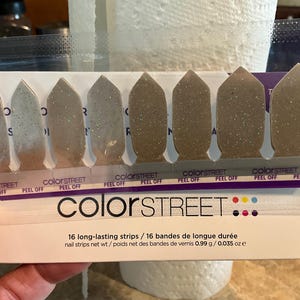 May include: Color Street nail strips in a package. The strips are various shades of gray with glitter. The package includes 16 long-lasting nail strips. The text "PEEL OFF" is visible on the package.