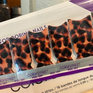 May include: Color Street nail strips with a leopard print design. The nail strips are orange and black. The packaging reads "HOST FOR BORING NAILS" and "PEEL OFF".