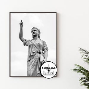 May include: Black and white photograph of a statue of a woman with her arm raised, pointing upwards. The statue is in a classical style, with the woman wearing a flowing robe. The background is a cloudy sky.