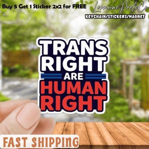 Könnte beinhalten: Ein Aufkleber mit dem Text "TRANS RIGHT ARE HUMAN RIGHT" in Weiß, Blau und Rot. Der Aufkleber wird von einer Hand vor einem verschwommenen grünen Hintergrund gehalten. Der Aufkleber ist 5,08 cm x 5,08 cm groß. Der Text "FAST SHIPPING" steht unten.