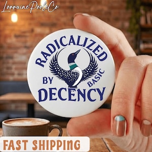 Może przedstawiać: Biały guzik z granatowym napisem "RADICALIZED BY BASIC DECENCY" i ilustracją nurka. Guzik trzymany jest w dłoni, z filiżanką kawy na pierwszym planie.