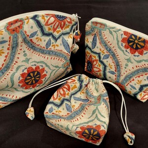 May include: Three fabric pouches with a white background and a colorful floral pattern. The pouches are different sizes and have drawstrings or zippers.