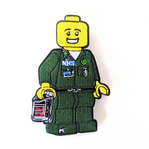 May include: Green and yellow embroidered patch of a Lego minifigure wearing a green uniform with the text "NHS" on the chest and a stethoscope around the neck. The minifigure is holding a red and white medical device.