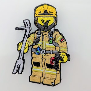 May include: Embroidered patch of a Lego minifigure firefighter wearing a yellow helmet, black beard, and a yellow and black fire suit. The minifigure is holding a grey crowbar.