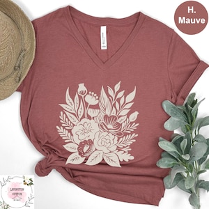 a red t-shirt with a white floral design, a straw hat, and some greenery, all arranged on a white background.