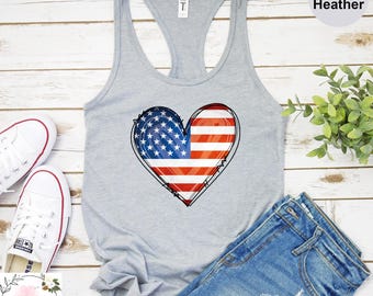 May include: Athletic heather gray tank top with a heart-shaped American flag design. The tank top is paired with denim shorts and white sneakers. The text "Athletic Heather" is visible in the image.